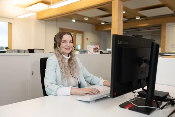Die Arbeit in der Administration/Verwaltung ist auf die Anforderungen einer Universität zugeschnitten. (Foto: UW/H | Michael Schwettmann) Eine junge Frau mit Headset sitzt vor einem Bildschirm und lächelt in die Kamera.
