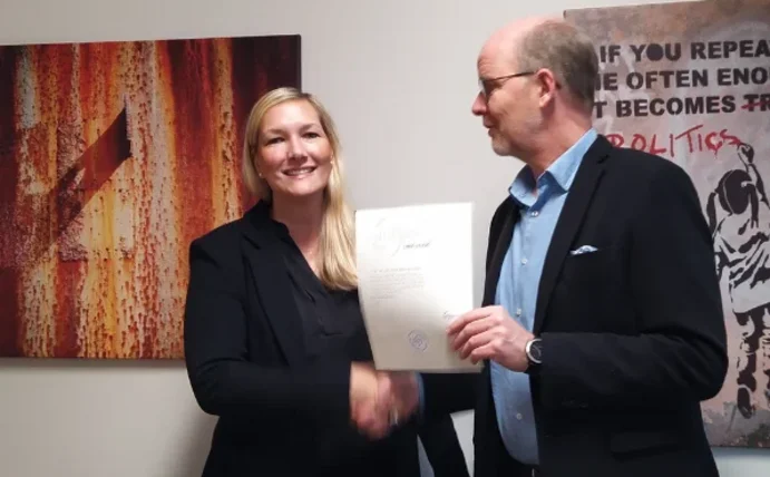 Ein Mann überreicht einer Frau eine Urkunde und schüttelt ihr die Hand.