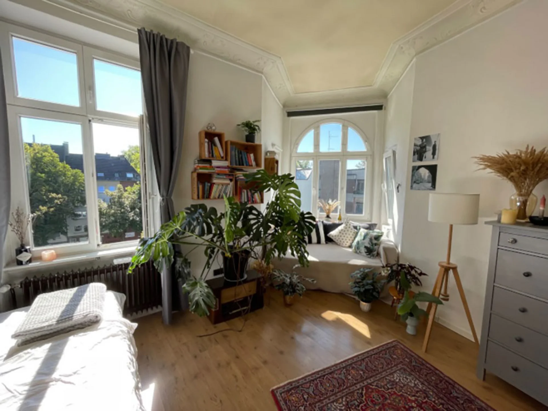 This is how students in Witten live (Photo: Private) A view inside a shared flat. There is a bed on the left and a chest of drawers on the right. A seating area has been set up in front of a large round window, with houseplants in front of it.