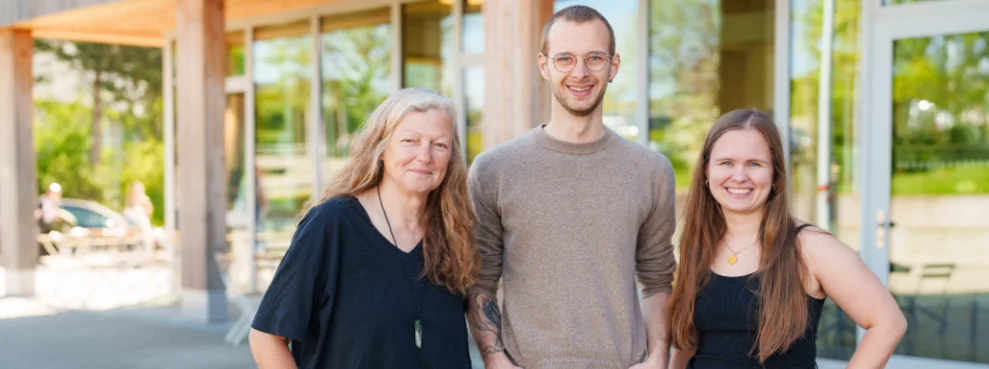 You see three people standing in front of the university, smiling at the camera. 