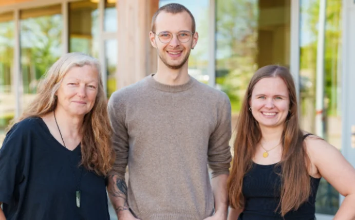 You see three people standing in front of the university, smiling at the camera. 