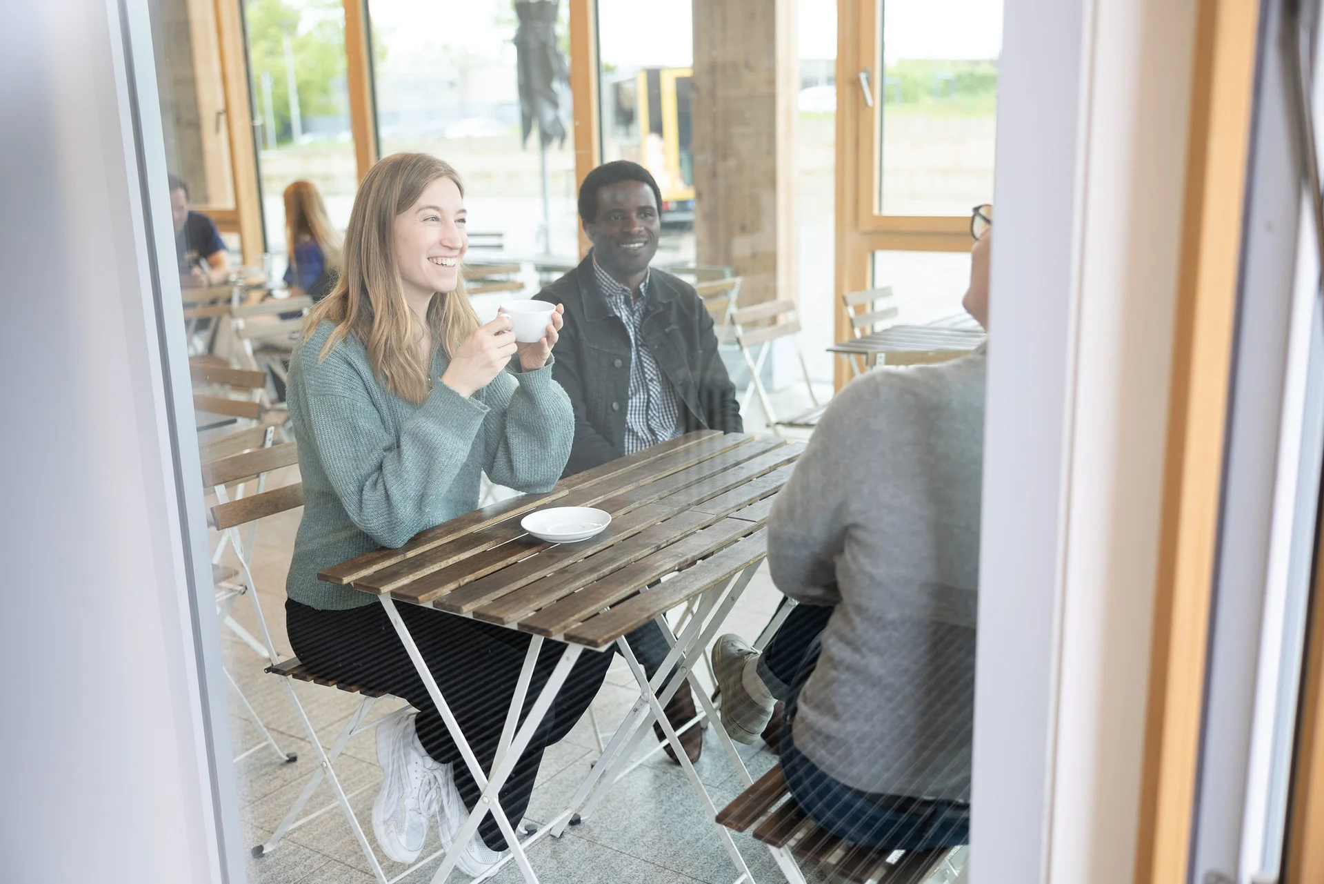 Drei Personen sitzen an einem Tisch, trinken Kaffee und unterhalten sich.
