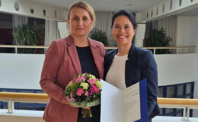 You see two women smiling warmly at the camera.