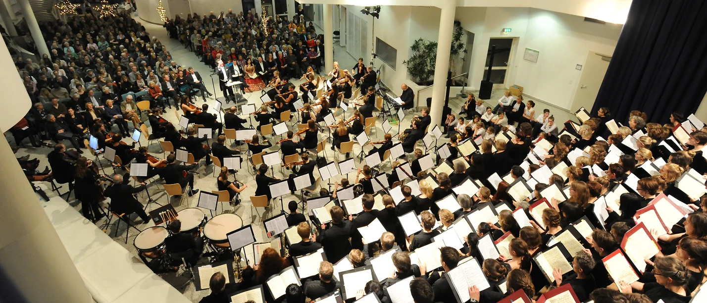 Giuseppe Verdi – Concert by the UW/H Choir and Orchestra (Photo: UW/H) A bird’s-eye view of the Witten/Herdecke University choir and orchestra ensemble in the university hall. In the foreground, a top-down view of the choir with their music open. In the middle section, the orchestra, and in the final third of the photo, part of the audience (Photo: UW/H)