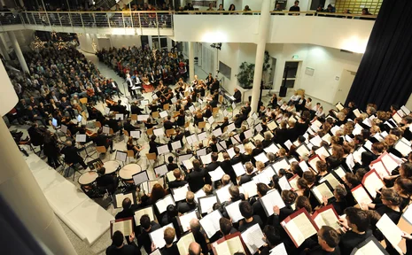 Giuseppe Verdi – Concert by the UW/H Choir and Orchestra (Photo: UW/H) A bird’s-eye view of the Witten/Herdecke University choir and orchestra ensemble in the university hall. In the foreground, a top-down view of the choir with their music open. In the middle section, the orchestra, and in the final third of the photo, part of the audience (Photo: UW/H)