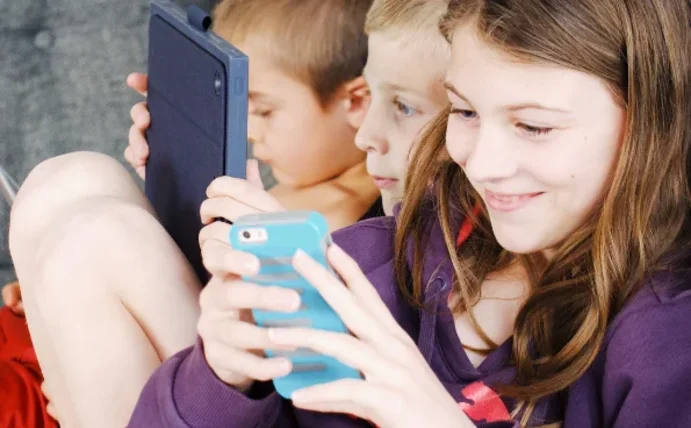 Drei Kinder sitzen mit Handys und Tablets auf dem Sofa.