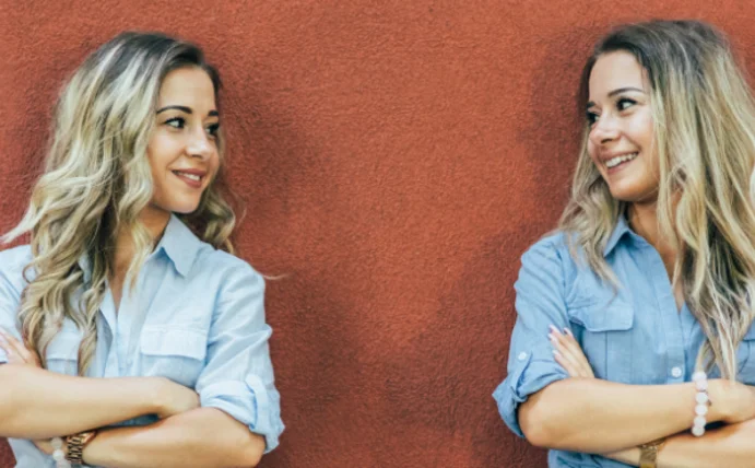 Zwei Frauen, die sich sehr ähnlich sehen, schauen sich an. Sie haben die gleiche Frisur, tragen ähnliche Kleidung und haben dieselbe Körperhaltung.