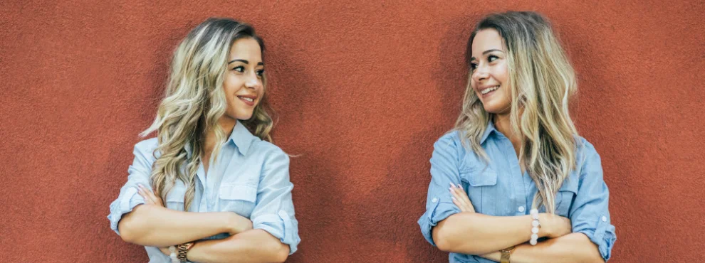 Zwei Frauen, die sich sehr ähnlich sehen, schauen sich an. Sie haben die gleiche Frisur, tragen ähnliche Kleidung und haben dieselbe Körperhaltung.