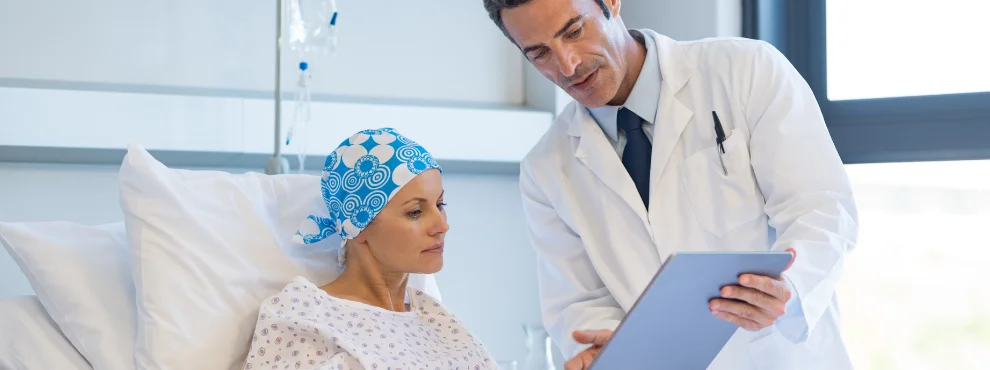 A doctor holds out a clipboard to a cancer patient and explains something to her.