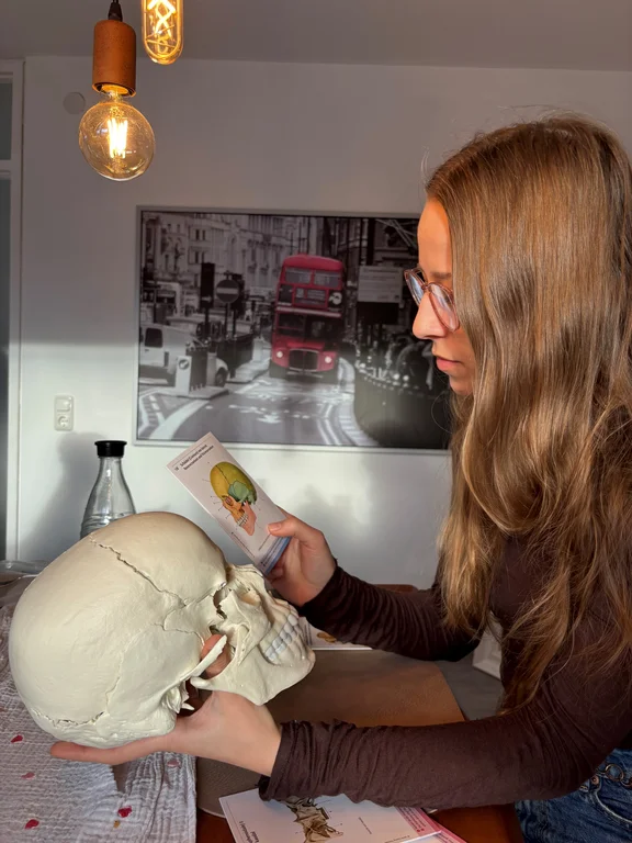 Alicia hält einen Schädel in der einen und eine Abbildung in der anderen Hand.