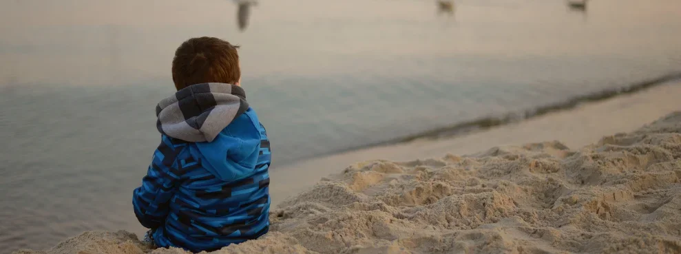 Ein Kind sitzt am Strand und schaut aufs Meer.