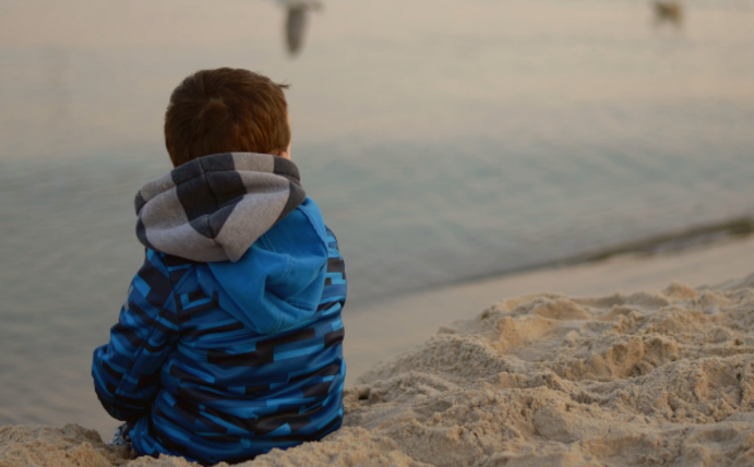 Ein Kind sitzt am Strand und schaut aufs Meer.