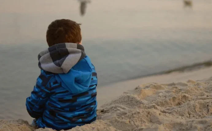 Ein Kind sitzt am Strand und schaut aufs Meer.