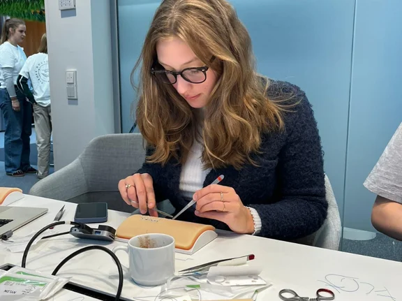 Pia hat sich mit dem Medizinstudium in Witten einen Traum erfüllt. (Foto: privat) Pia Klee sitzt an einem Tisch und übt Nahttechniken an einem Stück Kunsthaut.