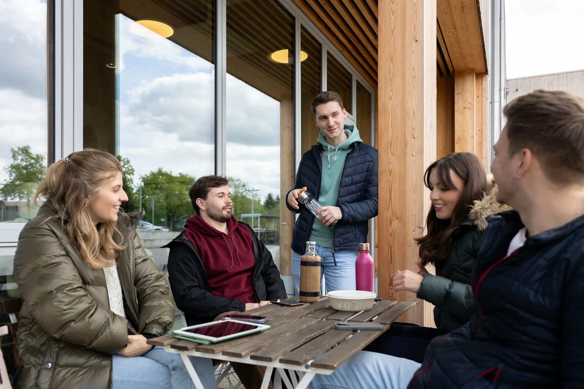 Relaxed break time between the seminars (Photo: UW/H | Michael Schwettmann) A group of students are sitting on a terrace in front of the university café and chatting.