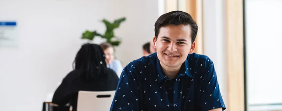 Bewirb dich für den Studiengang Management & Pschologie (B. Sc.) an der UW/H. (Foto: UW/H | Johannes Buldmann) Ein junger Mann sitzt an einem Tisch und hat ein Heft vor sich liegen.