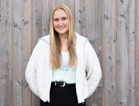 Bewirb dich für den Studiengang Psychologie (M. Sc.) an der UW/H. (Foto: UW/H | Michael Schwettmann) Eine junge Frau steht mit dem Rücken vor einer Gebäudewand aus Holz.