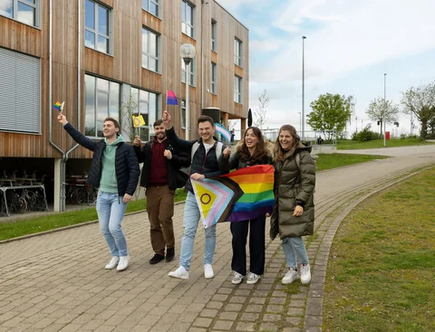 Gelebte Vielfalt ( Foto: UW/H | Michael Schwettmann) Eine Gruppe Studierender läuft mit geschwenkten Pride-Flaggen über dem Campus.