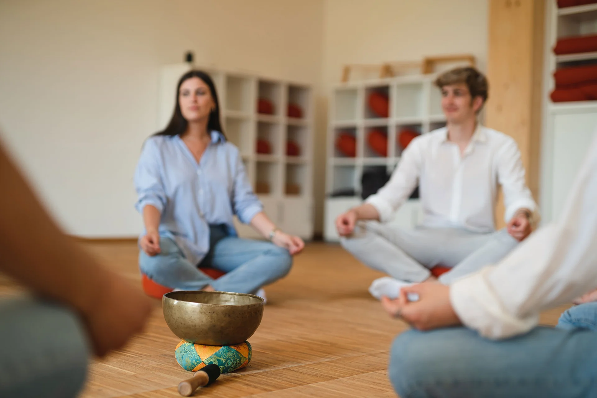 The focus is on two students sitting cross-legged on the floor. A singing bowl stands between them.