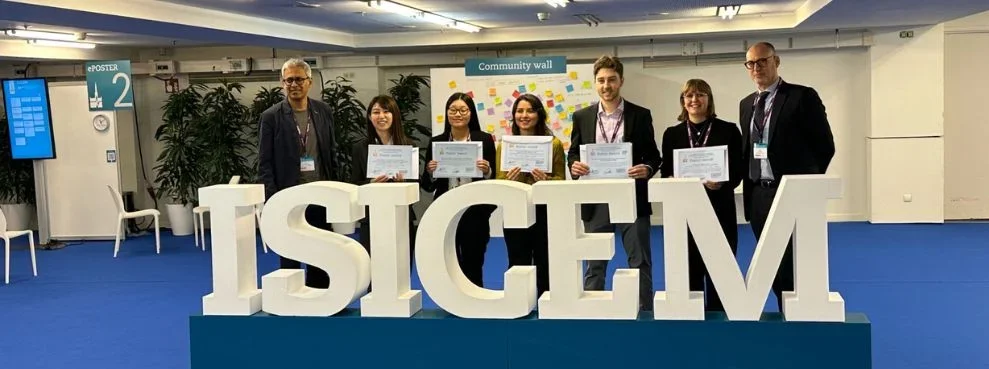 Sieben Personen, fünf davon mit Urkunden, posieren hinter einem großen ISICEM-Logo
