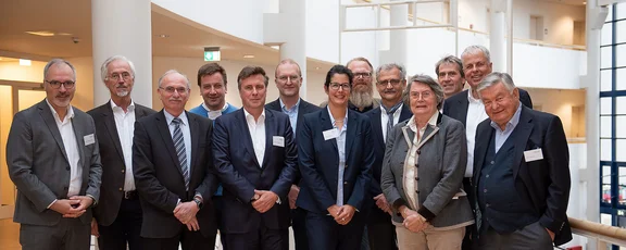 13 people stand next to each other and smile into the camera.