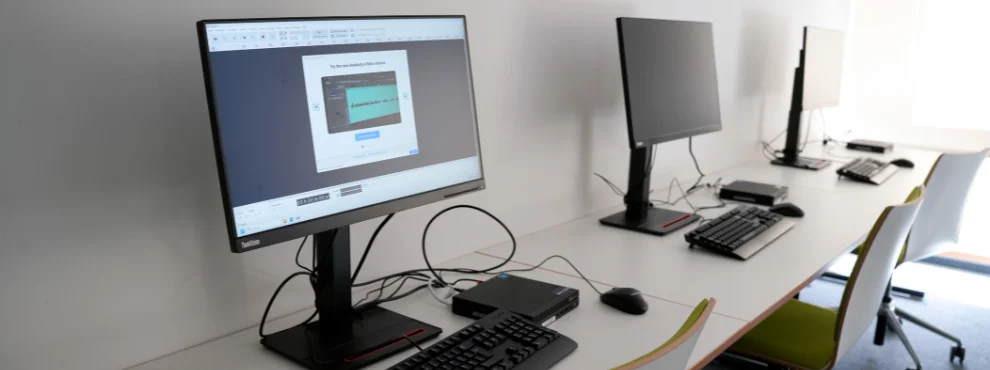 Drei Computerarbeitsplätze stehen in einer Reihe. Ein Bildschirm zeigt ein Audioschnittprogramm.