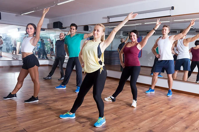 Zumba-Kurs (Foto: Canva) Eine Gruppe von Frauen und Männern tanzt in einer Sporthalle Zumba.