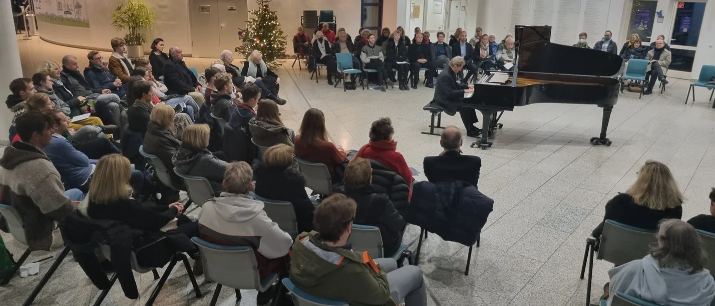 Traditionelles Nikolauskonzert mit Helge Antoni an der UW/H (Foto: UW/H | Britta Koch) Menschen sitzen in einer großen Halle und hören einem Klavierspieler zu.