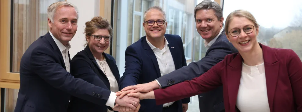 Five people hold their hands over each other and smile at the camera.