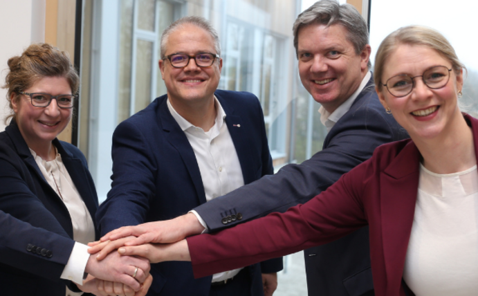 Fünf Personen halten ihre Hände übereinander und lächeln in die Kamera.