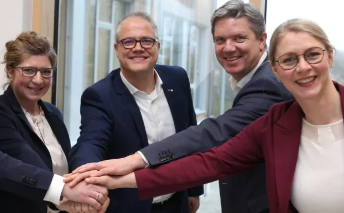 Fünf Personen halten ihre Hände übereinander und lächeln in die Kamera.