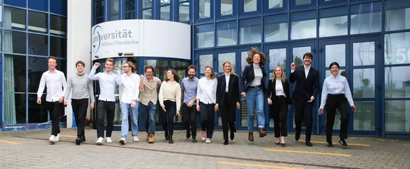 Bei uns zählen Motivation und Persönlichkeit (Foto: UW/H | Kristina Eichhorn) Eine Gruppe Studierender läuft vom Gebäude-Eingang der Universität lachend auf die Kamera zu.
