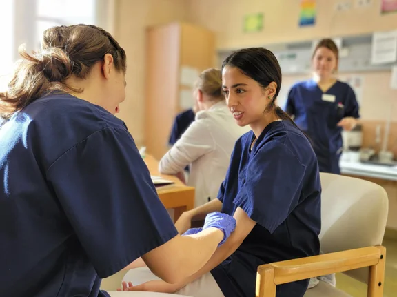 Zwei Studentinnen üben aneinander die korrekte Venenpunktion.