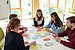 Four students are sitting at a table with a lecturer in a classroom. On this table are large, colorful circles with words written on them.