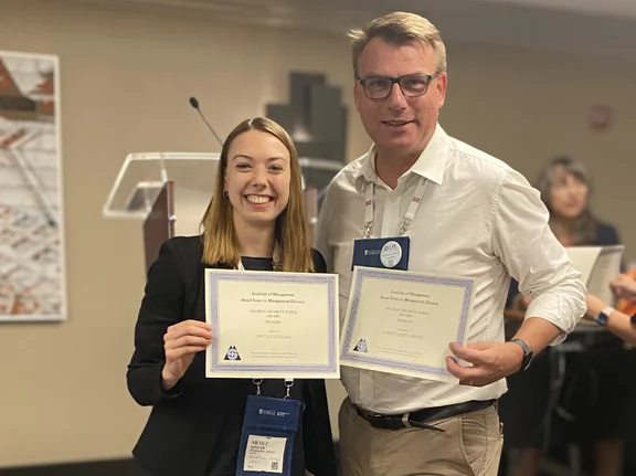 Nicole Stelle seht neben ihrem Betreuer Prof. Dr. Guido Möllering. Beide lächeln in die Kamera und halten eine Urkunde für das Best Student Paper 2024 in den Händen.