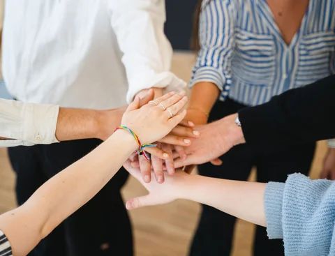 Our services (Photo: UW/H | Johannes Buldmann) People standing in a circle place their hands on top of one another.