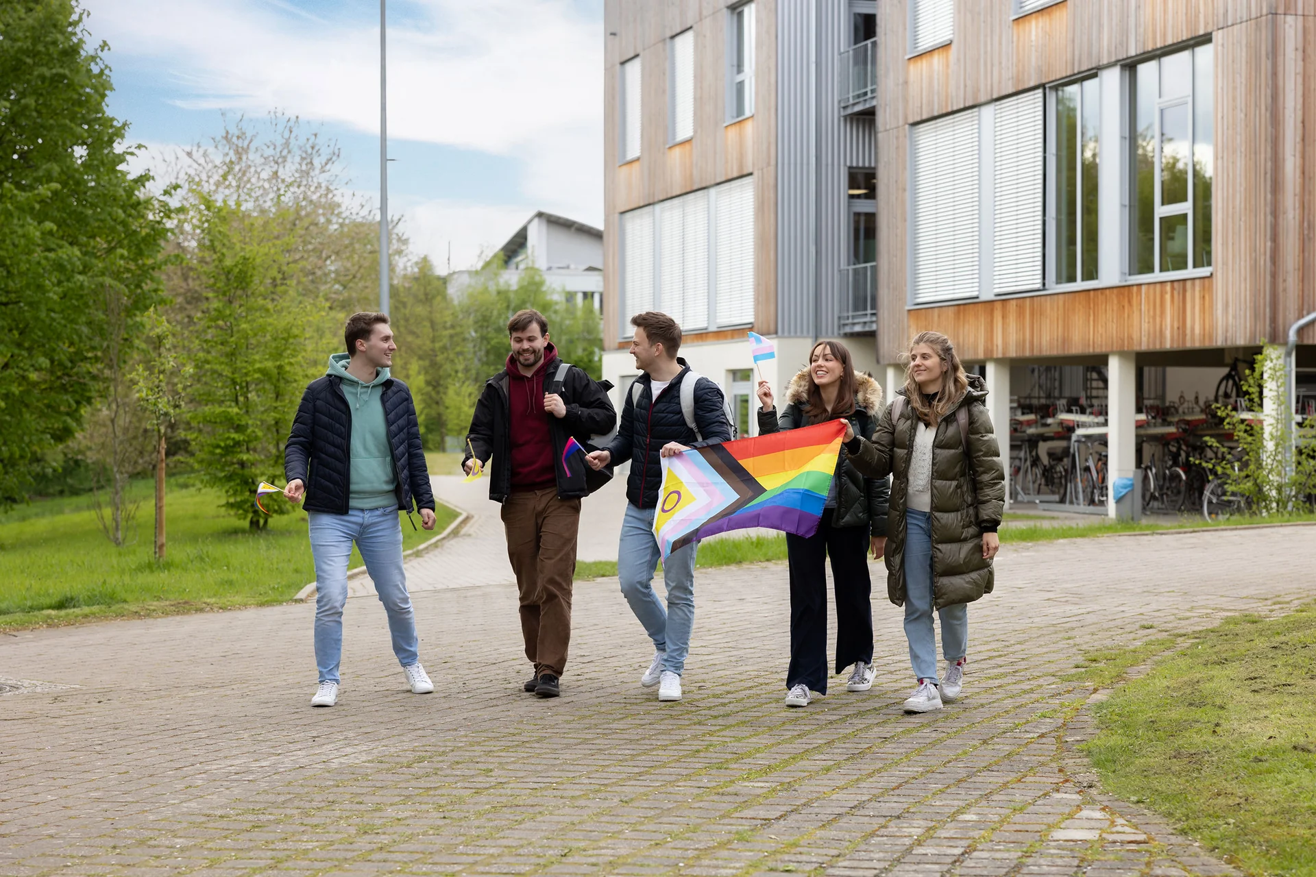 Für Toleranz und Vielfalt an der UW/H (Foto: UW/H | Michael Schwettmann) Eine Gruppe Studierender läuft mit schwenkenden Pride-Flaggen über den Campus.