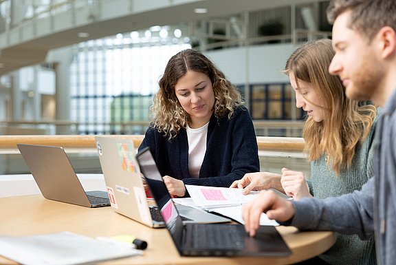 An der UW/H ist es uns wichtig, den wissenschaftlichen Nachwuchs zu fördern (Foto: UW/H | Michael Schwettmann) Drei junge Menschen sitzen an einem Tisch und schauen gemeinsam auf ihre Laptops.