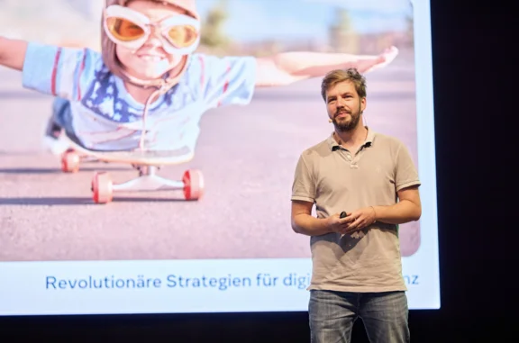 Daniel Verst steht vor einer Leinwand und hält einen Vortrag.