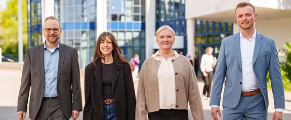 Die Universität Witten/Herdecke bietet zahlreiche Karrieremöglichkeiten in Lehre, Forschung, Verwaltung und anderen Bereichen an. (Fotos: UW/H) Vier Personen laufen nebeneinander über den Campus der Universität Witten/Herdecke.