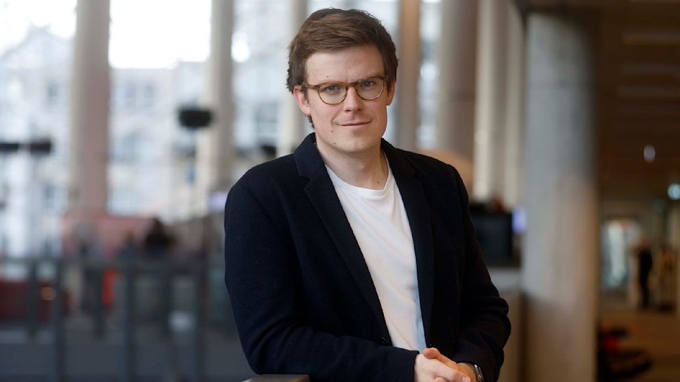 Max Matthey steht steht vor einem Cafe Hintergrund und guckt in die Kamera 