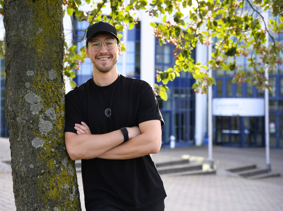 René Langenströer is completing the Master’s programme in General Management at UW/H. (Photo: UW/H | Miriam Kreimeyer) René Langeströer is leaning against a tree on the UW/H campus. Behind him is the university’s main building.