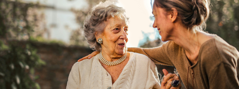 Eine junge und eine alte Frau geben einander die Hand und lachen sich an.