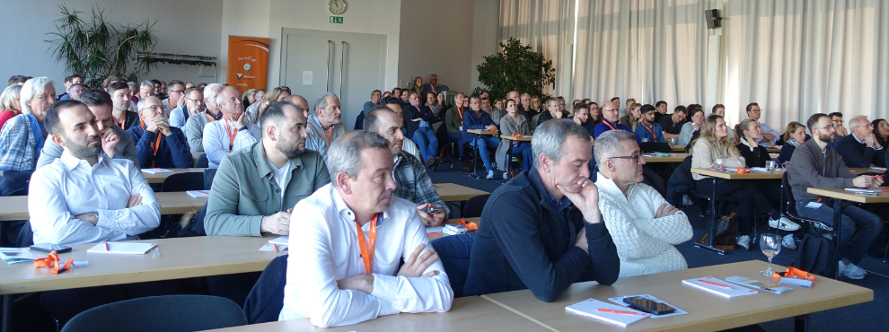 Many people sit at tables in a room, look ahead and listen.