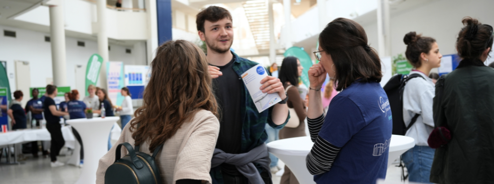 Beim Infotag haben Besucher:innen die Chance, die UW/H und das Campusleben kennenzulernen und sich über das Studienangebot zu informieren. (Foto: UW/H) Drei Personen unterhalten sich.