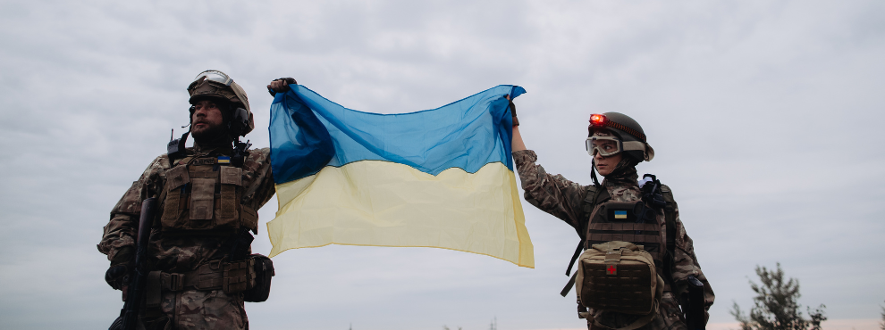 The war in Ukraine will continue. (Photo: Canva) A male soldier on the left and a female soldier on the right are holding a Ukrainian flag in their hands.