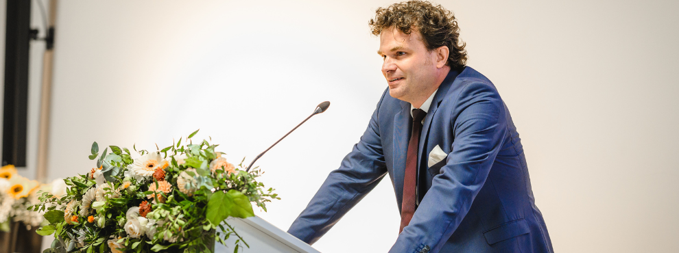 Prof. Dr. Christoph Schreiber ist neu im Herausgeberkreis der JR. (Foto: Van Laack| GRVBE Fotografie) Ein Mann im Anzug steht am Rednerpult.