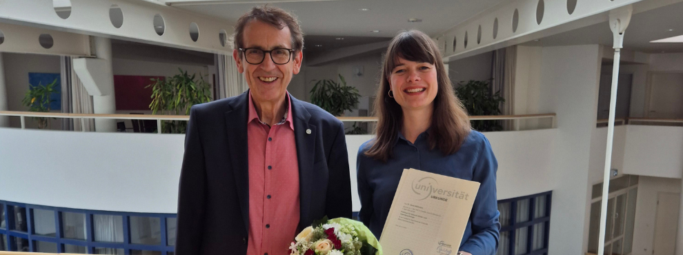 Prof. Dr. Anne Möllmann wurde auf die Professur für Klinische Kinder- und Jugendpsychologie an der Universität Witten/Herdecke berufen. (Foto: UW/H) Ein Mann und eine Frau stehen auf vor einer Brüstung der Universität Witten/Herdecke und lächeln in die Kamera. Die Frau hält ihre Berufungsurkunde in der Hand.