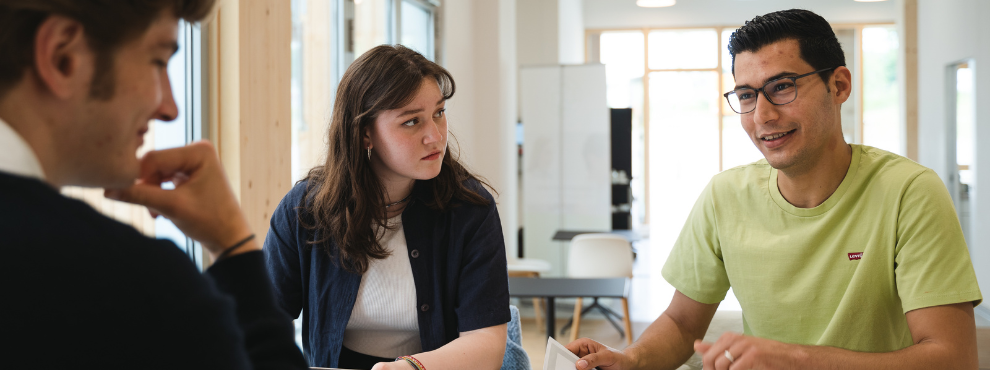 At UW/H, students discuss how they can help shape the economy and society responsibly. (Photo: UW/H I Johannes Buldmann) Three students in conversation in the new building